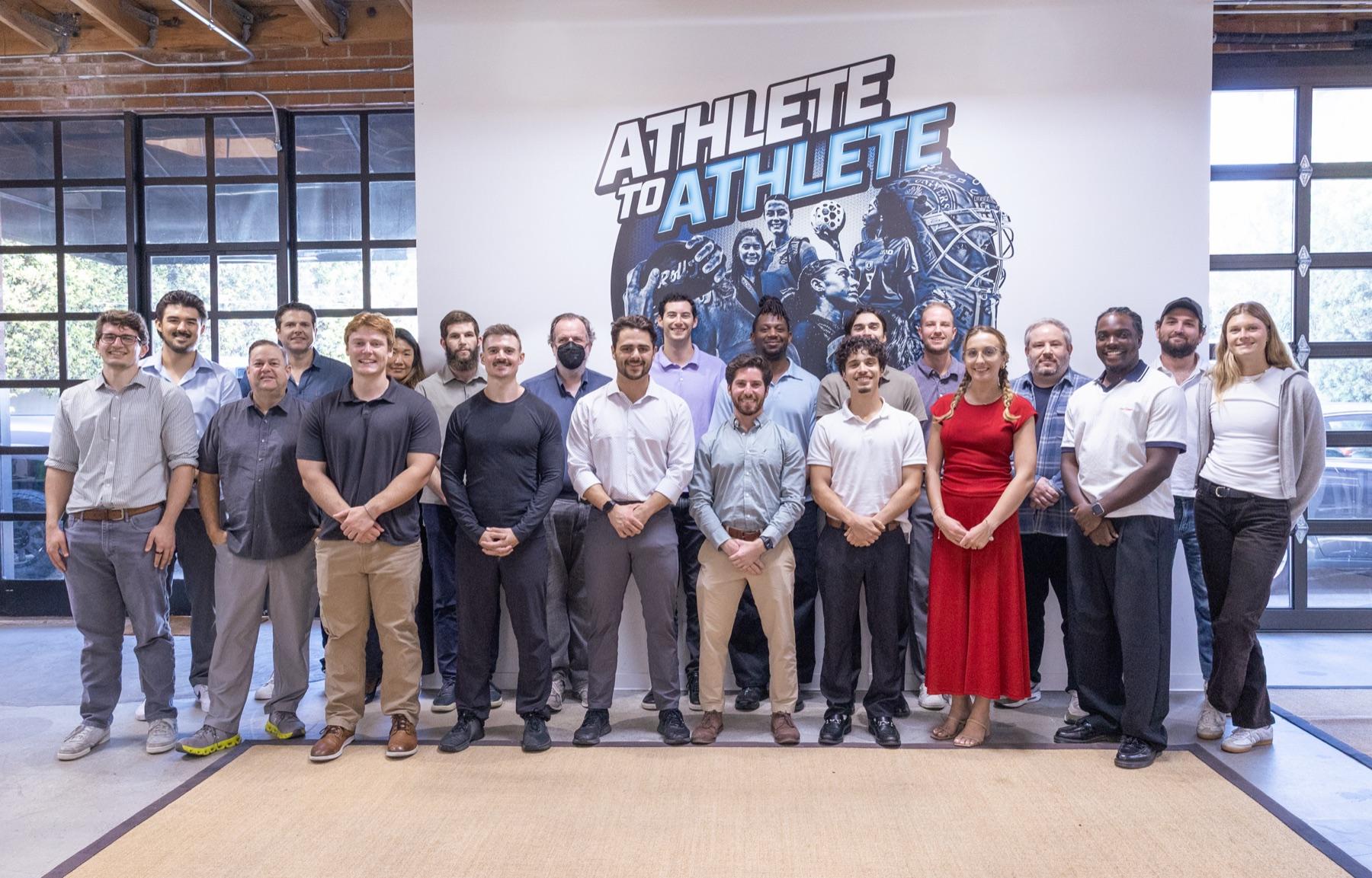 The Athlete To Athlete team in front of the Athlete To Athlete mural at the office